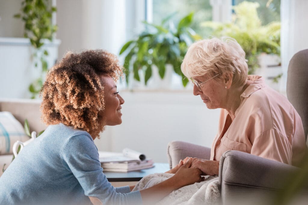 home nurse talking with senior woman, sitting in living room and holding her hands.